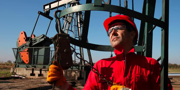 Oil and gas worker in red overalls inspecting a pump jack 
