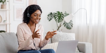 A woman taking a work call from her living room, using a laptop and headset 