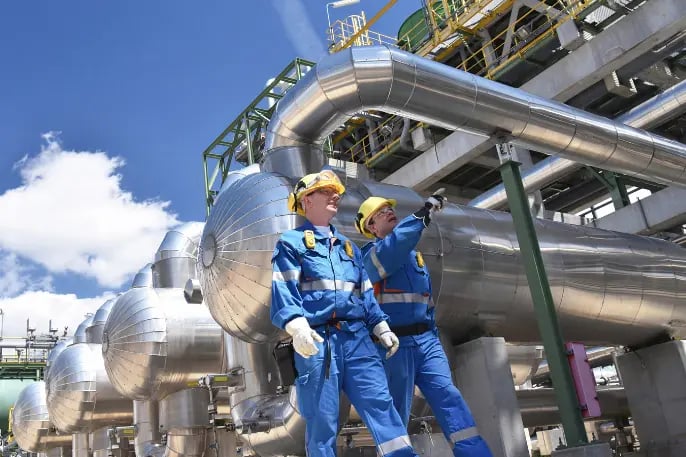 Oil and gas industry professionals in safety gear inspecting pipeline infrastructure at a processing plant