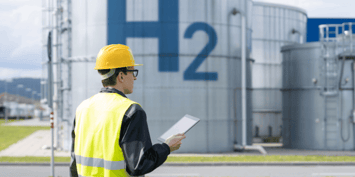 Worker in hi-vis and hardhat holding tablet in front of hydrogen tankers