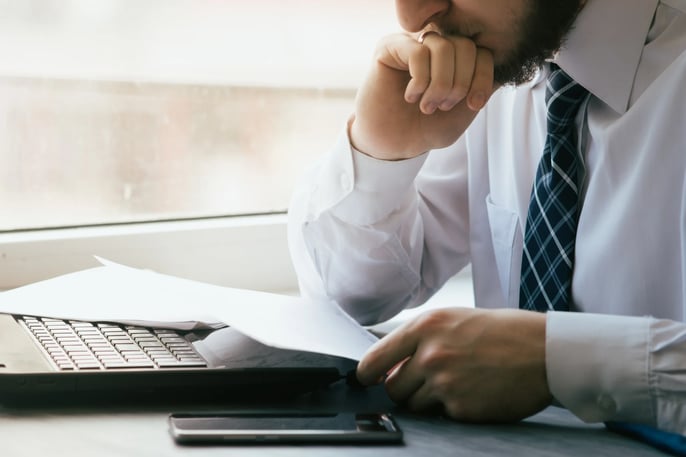 Man in suit reading papers on top of laptop