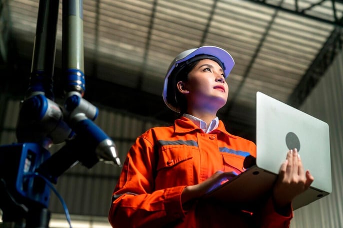 Female engineer in safety gear with a laptop, highlighting recruitment for advanced technology roles.