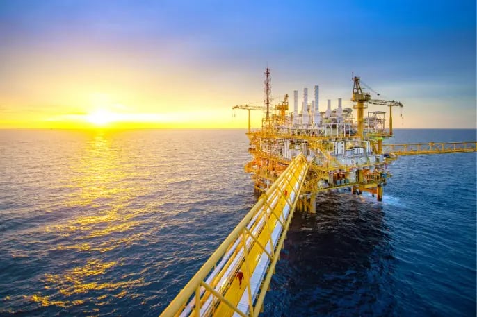 Offshore oil and gas drilling platform at sunset, with vast ocean horizon sun highlighting the structure