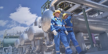 Two oil rig workers in safety gear inspecting pipelines