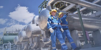 Two oil rig workers in safety gear inspecting pipelines 