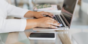 A pair of female hands with blue nail polist typing on a laptop keyboard